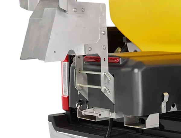 Close-up of a wessex snowex helixx spreader attached to the back of a pickup truck. The yellow spreader is secured with metal brackets and fasteners.